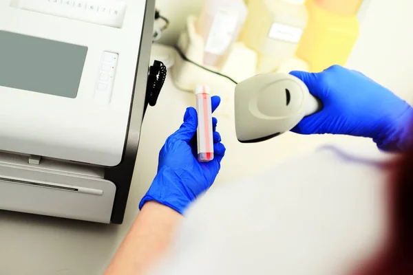 Медицинский техник в синих резиновых перчатках сканирует код пробирки в современной биохимической лаборатории. — стоковое фото