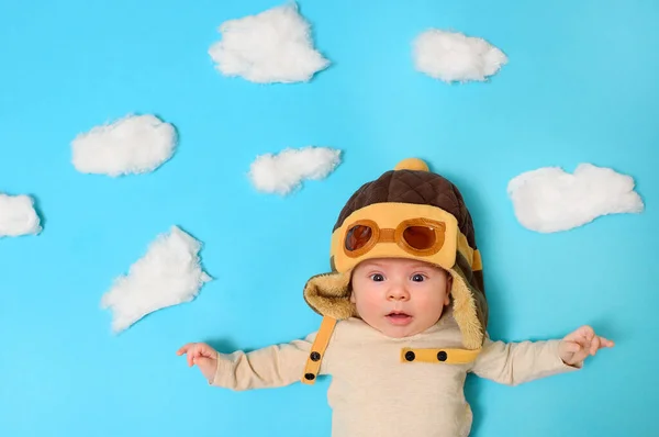 Baby in een piloten helm tegen een kunstmatige lucht en katoen wollen wolken. — Stockfoto