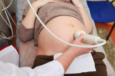 Doktor modern bir klinikte hamile bir kadının ceninini ultrason ile muayene ediyor..