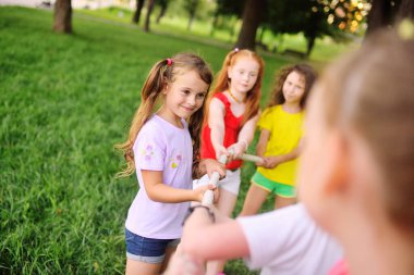 Bir grup anaokulu çocuğu - erkekler ve kızlar bir park ve yeşillik arka planında çekişme içinde.