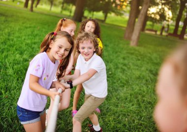 Bir grup anaokulu çocuğu - erkekler ve kızlar bir park ve yeşillik arka planında çekişme içinde.