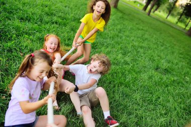 Bir grup çocuk açık havada çimenlerin ve parkın arka planına karşı bir çekişme içinde..