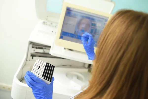 Un empleado de un laboratorio médico bacteriológico sostiene un recipiente con tubos de ensayo en sus manos contra el fondo del analizador. — Foto de Stock