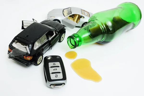 a broken toy car, a bottle with leftover alcohol and a car key on a white background.
