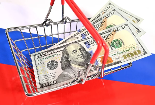 Kosár egy szupermarket amerikai dollárral a háttérben az orosz trikolor zászló. — Stock Fotó