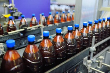 Bir bira fabrikasının arka planındaki taşıma bandındaki plastik bira şişeleri.