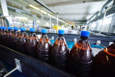 Bir bira fabrikasının arka planındaki taşıma bandındaki plastik bira şişeleri.