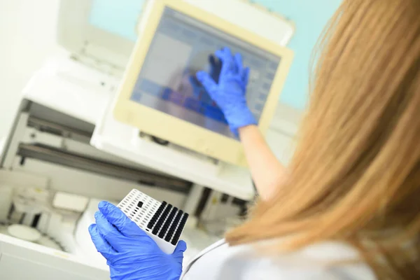 Pracownik medycznego laboratorium bakteriologicznego trzyma pojemnik z probówkami w rękach na tle analizatora. — Zdjęcie stockowe