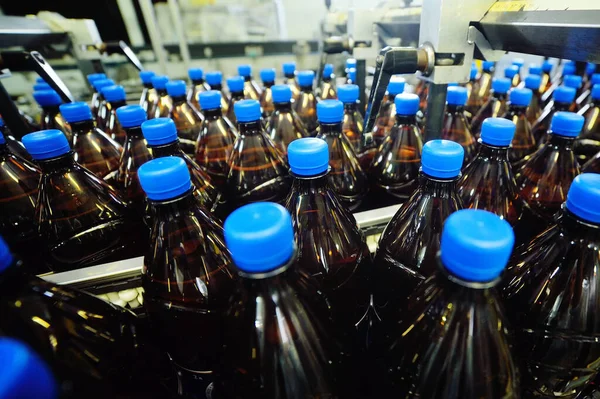 Plastikowe butelki PET z napojami lub piwem poruszają się na przenośniku taśmowym w tle fabryki. — Zdjęcie stockowe