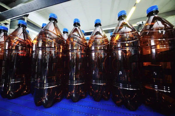 Botellas de plástico PET con bebidas o cerveza se mueven en una cinta transportadora en el fondo de la fábrica. —  Fotos de Stock