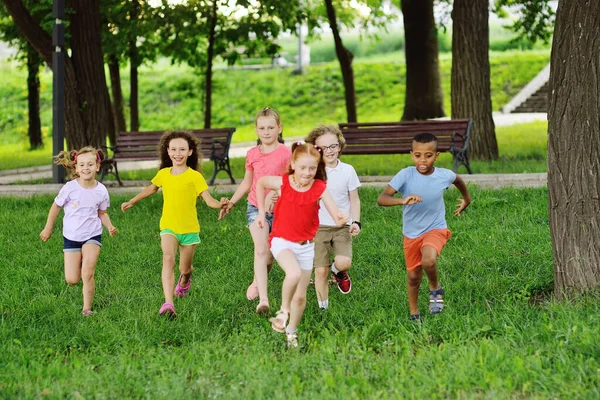 Grupo de crianças de meninos e meninas de diferentes raças estão correndo na grama verde contra o fundo de um parque de recreação. Dia das Crianças, — Fotografia de Stock