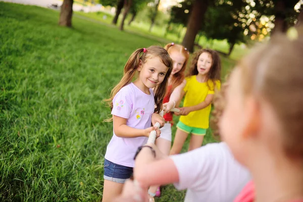 Un grupo de niños compiten en un tirón de la guerra al aire libre contra el fondo de la hierba y el parque. — Foto de Stock