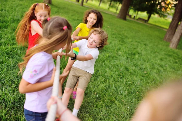 Grupp förskolebarn - pojkar och flickor tävlar i en dragkamp mot bakgrund av en park och grönska. — Stockfoto