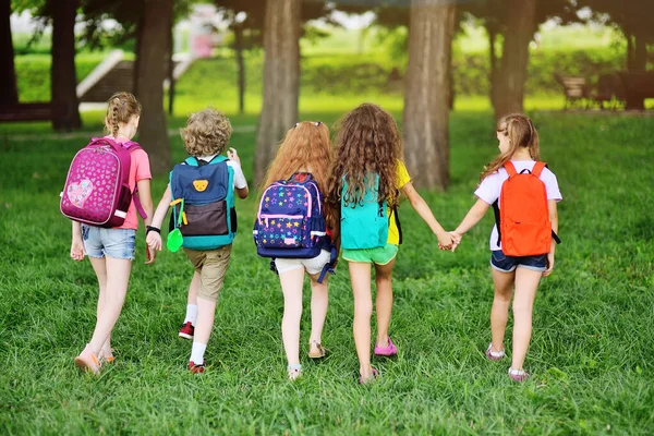 Sekelompok anak dengan ransel sekolah berjalan bergandengan tangan. Liburan, kembali ke sekolah, perkemahan musim panas. — Stok Foto