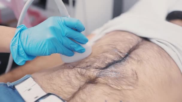 Médico en guantes de goma azul hace un ultrasonido de la cavidad abdominal a un hombre joven. — Vídeos de Stock
