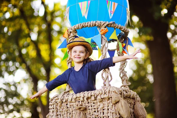 Симпатичная маленькая девочка в соломенной шляпе улыбается в корзине для воздушных шаров. — стоковое фото