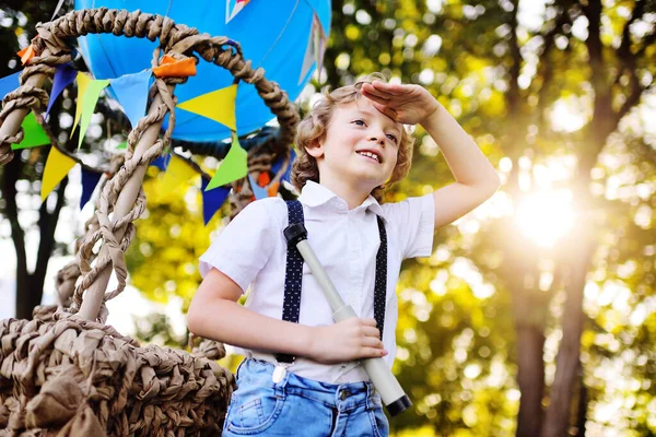 Elinde teleskopla mavi bir balon sepetinin arkasında gülümseyen kıvırcık saçlı küçük bir çocuk. — Stok fotoğraf