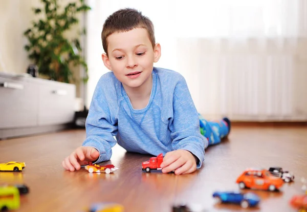 Маленький дошкольник, играющий в игрушечные машинки на деревянном полу в светлой комнате — стоковое фото
