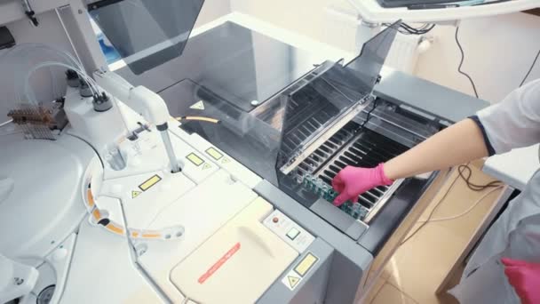 Una empleada de un laboratorio microbiológico moderno envía muestras de sangre a un analizador de sangre de laboratorio bioquímico. — Vídeo de stock