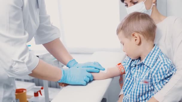 Anak kecil mengambil darah dari pembuluh darah untuk analisis. Anak itu duduk dalam pelukan ibunya di ruang manipulasi klinik.. — Stok Video