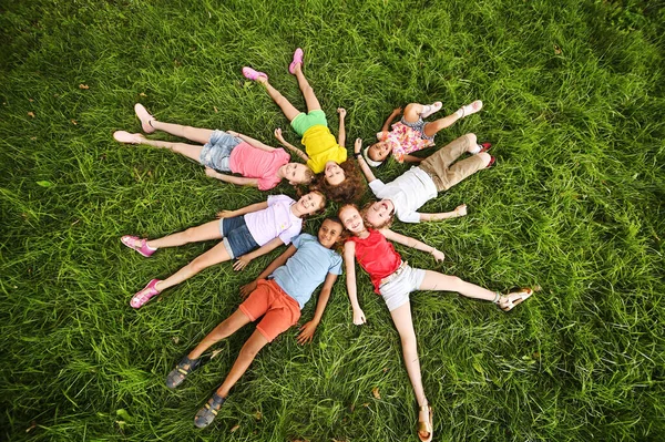 Farklı ırktan ve milletten çocuklar çimenlerin üzerinde renkli giysiler içinde uzanır ve gülümserler. Çocuk Günü — Stok fotoğraf