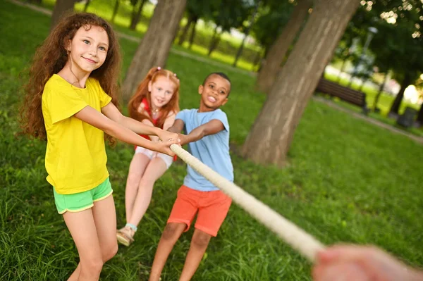 Grupp förskolebarn - pojkar och flickor tävlar i en dragkamp mot bakgrund av en park och grönska. — Stockfoto