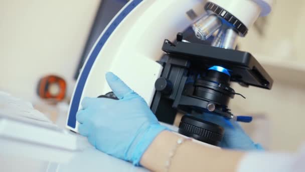 Ein Arzt in einer modernen Klinik arbeitet hinter einem fluoreszierenden Mikroskop. — Stockvideo