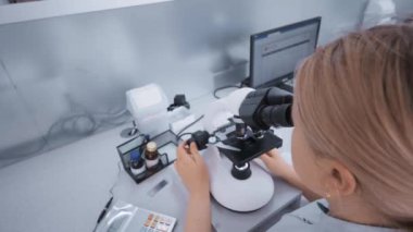 Modern bir klinikte çalışan bir doktor floresan uçlu bir mikroskobun arkasında çalışır..