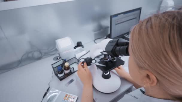 A doctor in a modern clinic works behind a fluorescent led microscope. — Stock Video
