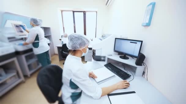Pracownicy laboratorium biochemicznego pracują przy komputerze i badają próbki na analizatorze hematologicznym. — Wideo stockowe