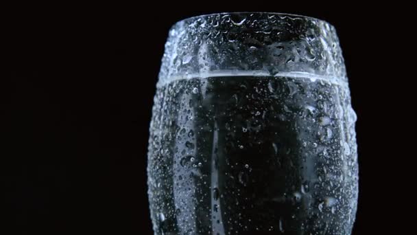 Glass or vase with water or with a transparent liquid with beautiful droplets on a glass close-up on a dark background. — Vídeo de stock