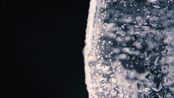 Glass or vase with water or with a transparent liquid with beautiful droplets on a glass close-up on a dark background. — Vídeo de stock