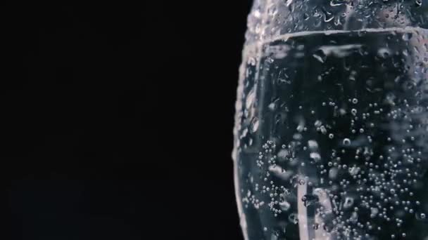 Zuiver natuurlijk mineraal koolzuurhoudend water wordt in een mooi glas gegoten. Druppels vloeistof stromen door het glas op een donkere achtergrond. — Stockvideo