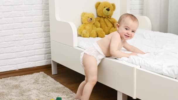 Baby boy in a diaper smiles gets off the crib and takes the first steps — Vídeos de Stock