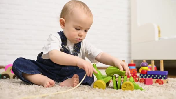 Boy in denim overalls sitting on the carpet playing toys — Stock Video