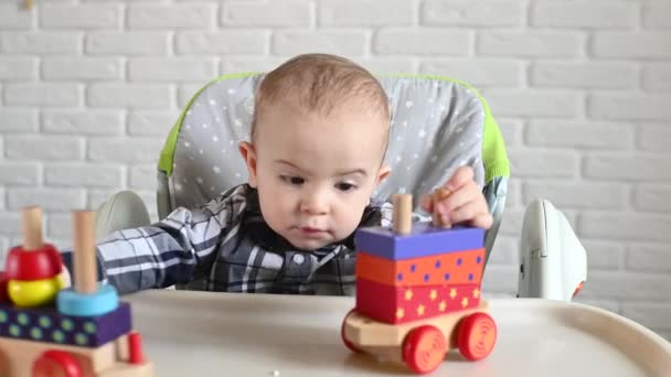 Niño sentado en una mesa de niños jugando con un tren de madera — Vídeo de stock