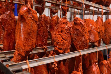mouth-watering pieces of pork delicacies in paprika and seasonings are hung on a metal rack in a meat-packing plant or butchers shop.