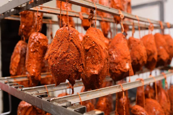 mouth-watering pieces of pork delicacies in paprika and seasonings are hung on a metal rack in a meat-packing plant or butchers shop.