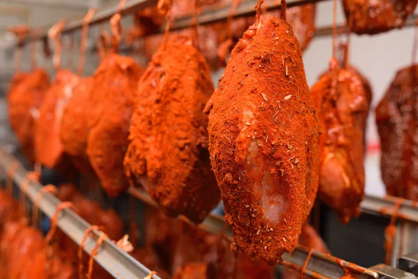 mouth-watering pieces of pork delicacies in paprika and seasonings are hung on a metal rack in a meat-packing plant or butchers shop.