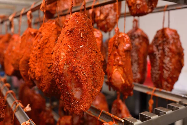 mouth-watering pieces of pork delicacies in paprika and seasonings are hung on a metal rack in a meat-packing plant or butchers shop.