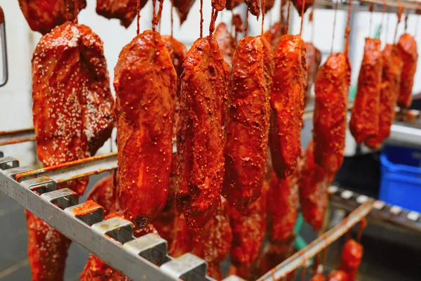 appetizing pieces of pork meat in a tomato marinade sprinkled with sesame seeds hang on a rack against the backdrop of a meat processing plant.
