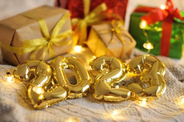 Noel hediyelerinin ve Noel ışıklarının arka planında ekose örülmüş altın numaralar 2023.