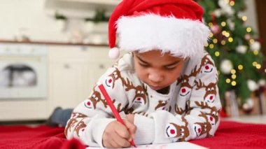 Noel Baba şapkalı bir çocuk rüya gibi gülümsüyor ve Noel Baba 'ya beyaz bir çarşafa bir mektup yazıyor. Bir Noel ağacının arka planında bir dilek listesi..