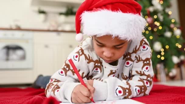 Een Jongetje Een Kerstmuts Liggend Een Ruit Glimlacht Dromerig Schrijft — Stockvideo