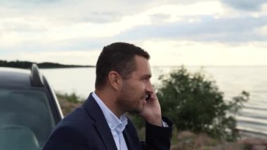 Bir iş adamı gölün kıyısında, denizde ya da okyanusta arabasının yanında durur, telefonda konuşur, işinde yeni başarılar elde etmekten mutludur.