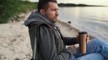 Bir adam göl, okyanus ya da deniz kıyısında bir araba gezisinde dinleniyor. Katlanan sandalyede oturuyor..