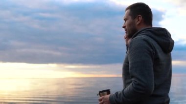 İnsan, deniz ya da okyanus yakınlarındaki geniş bir sahilde telefonla konuşuyor. Suda gün batımı.