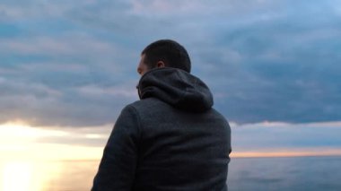 İnsan, deniz ya da okyanus yakınlarındaki geniş bir sahilde telefonla konuşuyor. Suda gün batımı.