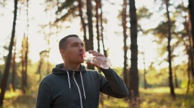 Ormanda ya da parkta koşudan sonra plastik atık şişesinden su içen bir adam.