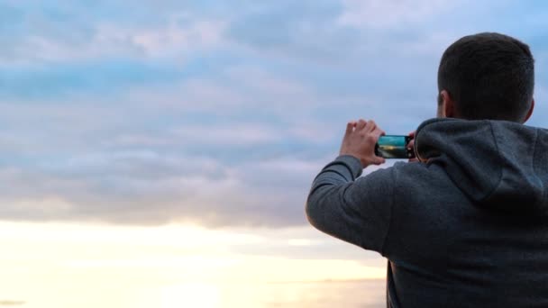 Un bărbat fotografiază apusul soarelui sau face un videoclip pe mare la telefon — Videoclip de stoc